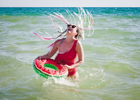 A cheerful middle-aged woman with a watermelon wedge swimming circle swimming in a sea. The concept of leisure and entertainmentの写真素材