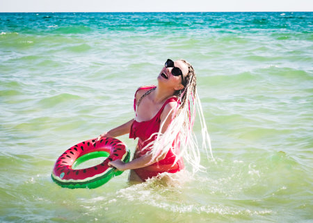 A cheerful middle-aged woman with a watermelon wedge swimming circle swimming in a sea. The concept of leisure and entertainmentの写真素材