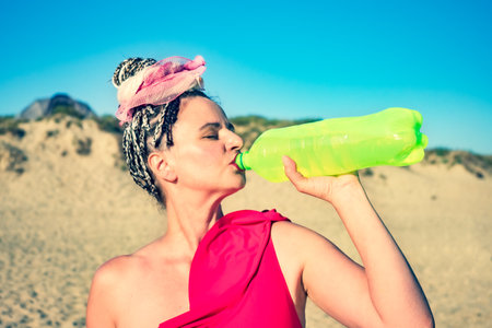 Side view portrait of middle-aged woman drinking a vegetable soda in a bottle on a beachの写真素材