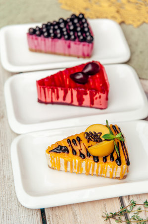 three triangular creative pieces of cake with apricot plum and currant berry in cafe on wooden...