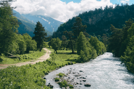 Highland landscape with road and river with green pine forest and mountainds at backgroundの写真素材