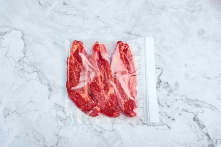 raw beef steaks in vacuum package at white marble background. Copy spaceの写真素材