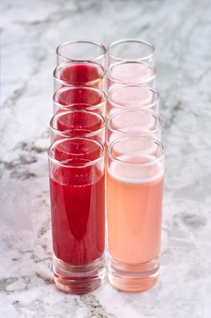 two rows of alcohol shot cocktails. coral and red colored drinks. vertical