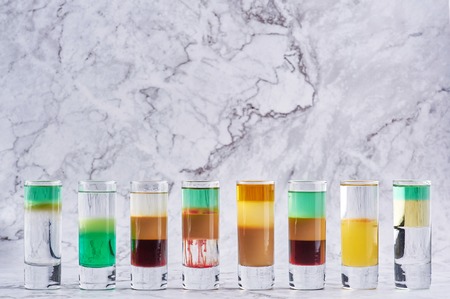 row of eight different alcohol shot cocktails at marble backdrop. Copy spaceの写真素材