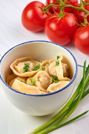 dumplings with parsley and onion at white wooden table top. Pelmeni - traditional russian cuisine dish dough with minced meat inside. decorated with tomatoesの写真素材