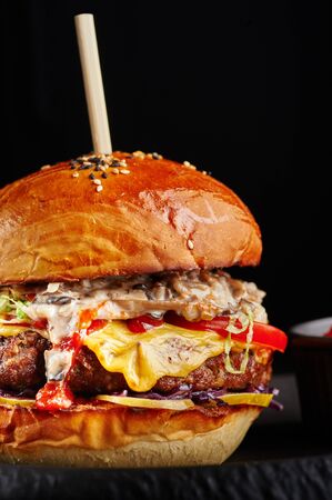 perfect burger with big beef cutlet, cheese, tomatoes, mushroom sauce and ketchup at black background with copy space.の写真素材