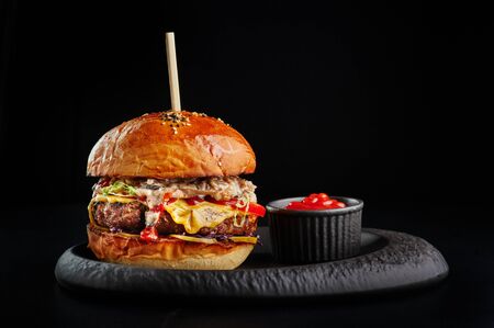 perfect burger with big beef cutlet, cheese, tomatoes, mushroom sauce and ketchup at black background with copy space.の写真素材