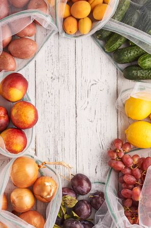 Frame of fruits and vegetables in reusable eco bags at white wooden background. Recycled bags instead of plastic bags. Plastic free. Vertical. Top view Flat lay with copy spaceの写真素材