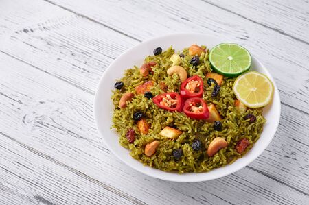 Palak Paneer Biryani at white wooden background. Palak Paneer Biryani is vegetarian indian cuisine dish with spinach, paneer cheese, basmati rice, spices, nuts and raisins. Copy Spaceの写真素材