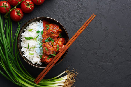 Chicken Manchurian in bowl with basmati rice at black concrete background. Chicken Manchurian is...