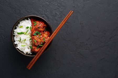 Chicken Manchurian in bowl with basmati rice at black concrete background. Chicken Manchurian is Indian Chinese cuisine dish with Chicken breasts, bell pepper, tomatoes, soy sauce. Copy spaceの写真素材