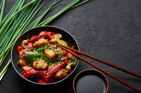 Schezwan Chicken or Dragon Chicken in black bowl at dark slate background. Szechuan Chicken is popular indo-chinese spicy dish with chilli peppers, chicken and vegetables.の写真素材