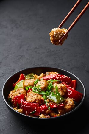 Schezwan Chicken or Dragon Chicken in black bowl at dark slate background. Szechuan Chicken is popular indo-chinese spicy dish with chilli peppers, chicken and vegetables.の写真素材