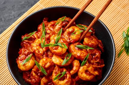 Schezwan Prawns in black bowl at dark slate background. Schezwan Prawns is indo-chinese cuisine curry dish with prawns or shrimps roasted in Schezwan Sauce.の写真素材