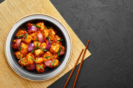 Schezwan Paneer in black bowl at dark slate background. Schezwan Paneer is indo-chinese cuisine dish...