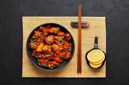 Fish Manchurian dry looks like Schezwan Fish in black bowl at dark slate background. Fish Manchurian - is indo chinese cuisine dish with deep fried salmon, bell peppers, sauce and onion. Top viewの写真素材
