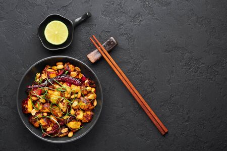 Kung Pao Paneer at black slate background. Kung Pao Paneer is a vegetarian version of chinese sichuan dish Gong Bao with paneer cheese, peanuts, chilli peppers, sauces and onion. Top view. Copy spaceの写真素材