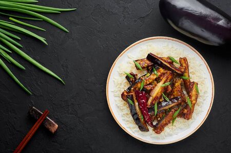 Sichuan Eggplant Stir Fry in black bowl at dark slate background. Eggplant Stir Fry is chinese cuisine dish with deep fried eggplant, chilli pepper, different sauces. Copy space. Top viewの写真素材