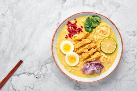 Ohn No Khao Swe on white marble background. Oh No Khao Suey is Coconut Milk Noodle Soup of myanmar cuisine with chicken meat and eggs. Burmese food. Top view. Copy spaceの写真素材