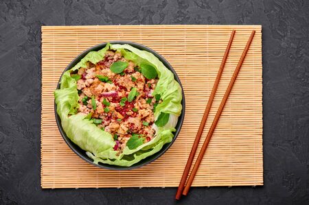 Laab Gai - Thai Minced Chicken Salad in black bowl at dark slate background. Larb is thailand cuisine dish with minced meat, fish sauce, lime juice, mint, lettuce and roasted rice. Thai Foodの写真素材
