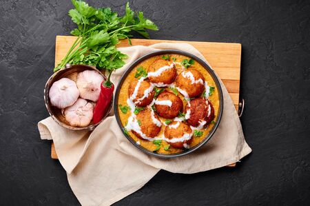 Malai Kofta Curry in black bowl at dark slate background. Malai Kofta is indian cuisine dish with potato and paneer cheese deep fried balls in onion tomato gravy with spices. Indian Food.の写真素材
