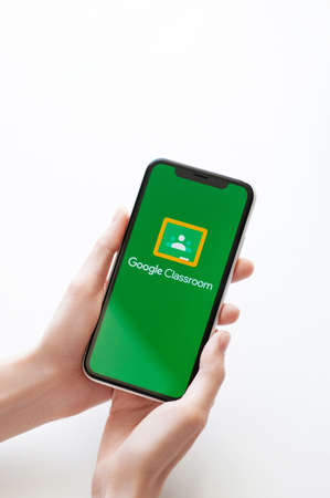 Moscow, Russia, 28 April, 2020. Google Classroom application logo on screen of Iphone X on white backdrop. Google Classroom app icon on smartphone display. Female hands keeps a phoneのeditorial素材