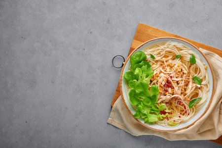 Guay Tiew Gai Cheek or Thai Chicken Noodle Soup in white bowl on gray concrete backdrop. Guay Tiew...