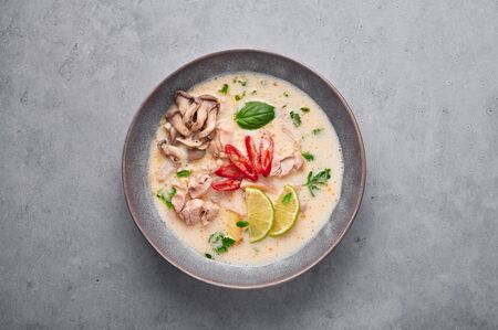 Tom Kha Gai or Thai Coconut Chicken Soup in matte gray bowl on concrete backdrop. Tom Kha Gai is Thailand cuisine dish with coconut milk, chicken, galangal, lemongrass, mushrooms, lime. Thai Foodの写真素材
