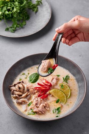 Tom Kha Gai or Thai Coconut Chicken Soup in matte gray bowl on concrete backdrop. Tom Kha Gai is Thailand cuisine dish with coconut milk, chicken, galangal, lemongrass, mushrooms, lime. Thai Foodの写真素材