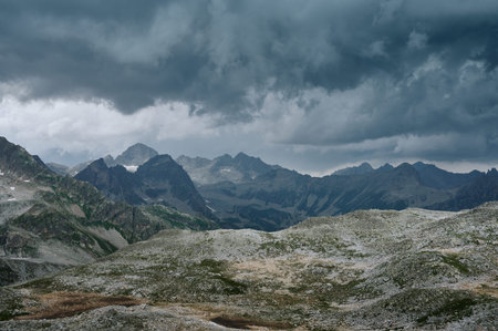 Gloomy mountain landscape with thunder cloudy sky, rocky ranges and peaks with glaciers and snow...