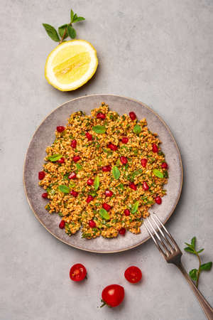 Kisir on gray plate on concrete table top. Turkish cuisine bulgur and parsley salad dish with pomegranate. Turkish food and meal. Top view.の写真素材