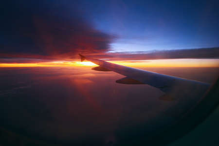 Beautiful sunrise in the sky during the flight. Plane wing above the cloudy colorful sunsetの写真素材