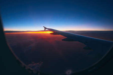 Beautiful sunrise view through the porthole during the flight. Plane wing above the cloudy colorful sunsetの写真素材