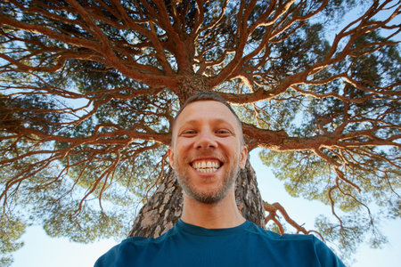 Happy laughing man in nature under the big tree. A man with a smile under the tree crown.