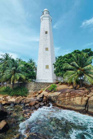 A white Dondra Head Lighthouse among the green palms on the rocky oceanic coast. Hidden gem of Sriの写真素材