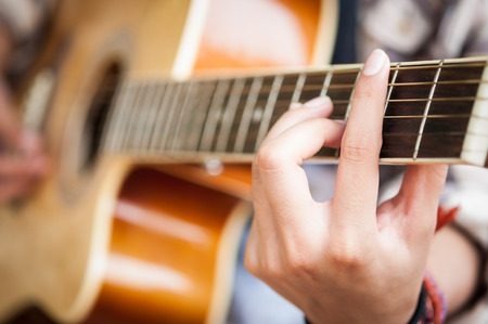 Closeup of young woman's hands playing acoustic guitar outdoorsの写真素材