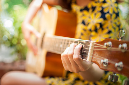 Closeup of young woman's hands playing acoustic guitar outdoorsの写真素材