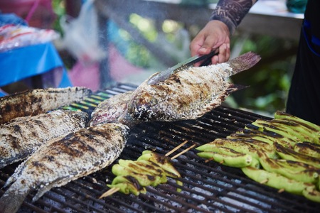 A hand grilling fish on smokey charcoal sieveの写真素材