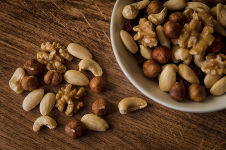 nuts, in a white bowl, fried on a dark wood background, blend of walnuts, almonds and roasted nuts, top viewの写真素材