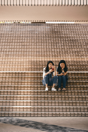 TSIM SHA TSUI, HONG KONG - APRIL 01, 2018 : Unidentified women using a smart phone sitting on steps at Hong Kong Cultural Centre in Tsim Sha Tsui.のeditorial素材