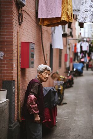 SHANGHAI, CHINA - MAY 18, 2019 : Unidentified old woman walking near her house with drying clothes outside on the clothes line near Liaoning Road in Shanghai, China.のeditorial素材
