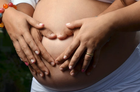 Pregnant woman with fingers Heart symbol and cute heart shaped in pregnant belly