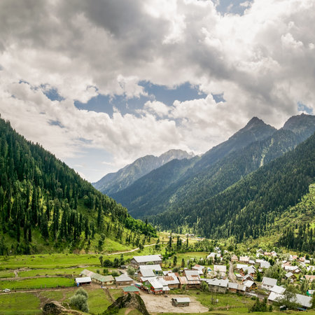 The breathtakingly beautiful Aru valley in Anantnag District of Jammu  Kashmir, India. The majestic mountains, lush green meadows, white clouds in blue sky and a hamlet and a meandering narrow road.の写真素材