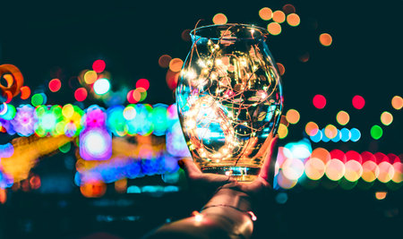 Beautiful abstract of bokeh effect of festive lights through a glass jar on the hand at twilight,...