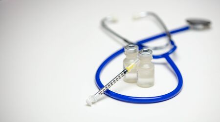 An empty syringe on two medical vials with a blue stethoscope in the background.の写真素材