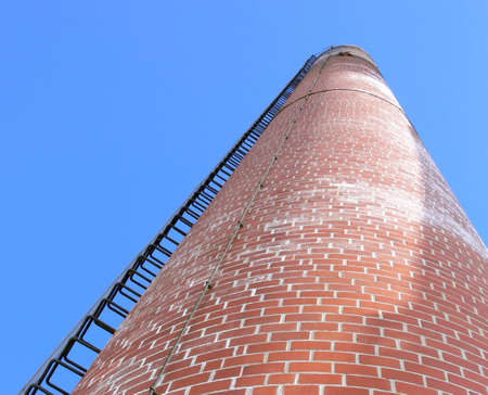 Photo of a chimney stack with a ladder running up the side. The photo is taken from the bottom looking up, with a blue sky in the background. Photo was taken in Selkirk, Manitoba, Canada.の写真素材