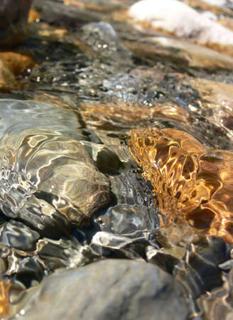 Close-up of clear water running over colourful rocks and pebbles in a stream.の写真素材