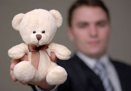 Young businessman holding teddy bear towards the camera. Shallow depth of field.の写真素材