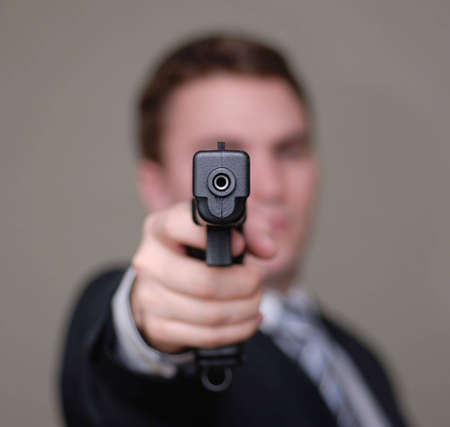 Young businessman pointing a gun towards the camera. Shallow depth of field.の写真素材