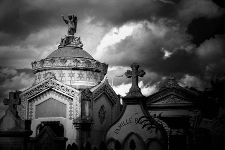Black and white image of a stone mausoleum and tombstones iin an ancient cemetery in France. Image...